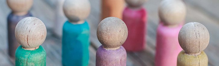 Bunte Holzspielfiguren in einer Gruppe auf einem rustikalen Holzuntergrund.