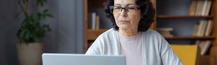 Eine Frau sitzt an einem Schreibtisch und recherchiert am Computer.